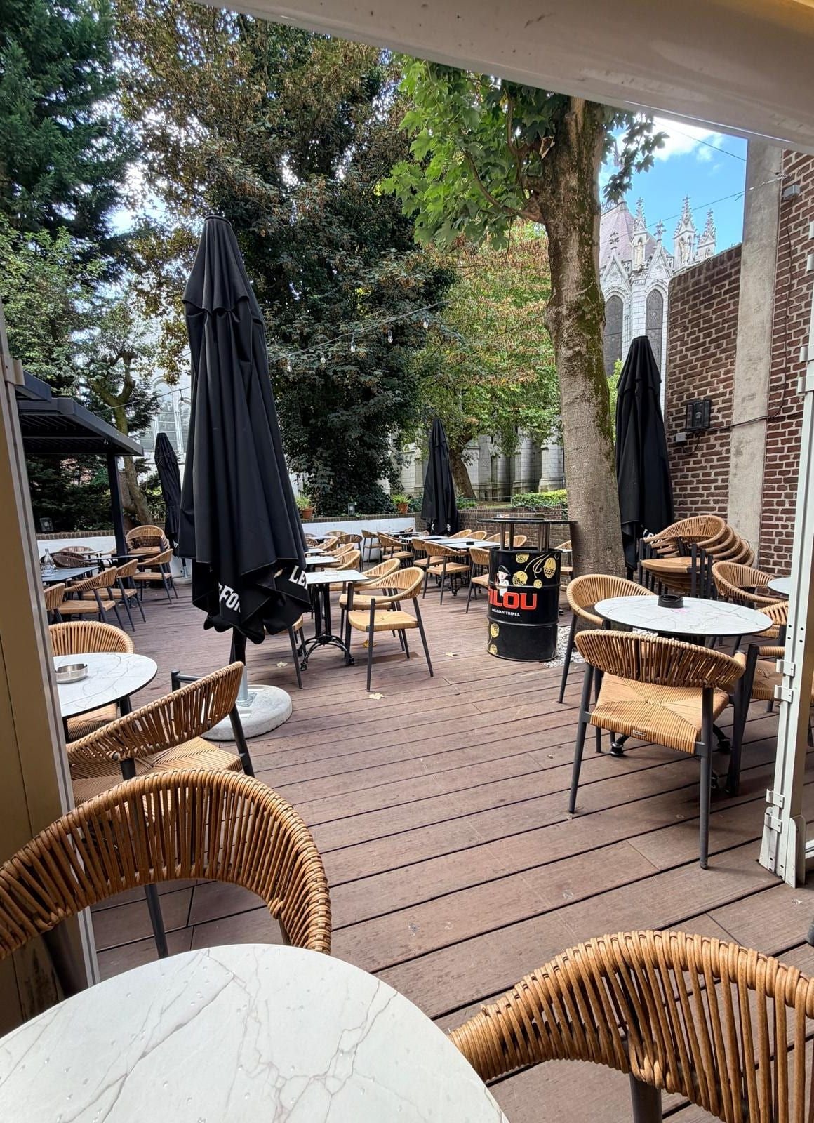 Vue d'ensemble de la terrasse : deck en bois, fauteuils en rotin, parasols et flèches de la cathédrale en arrière-plan